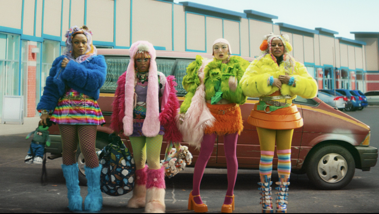 Keke Palmer, Taylour Paige, Naomi Ackie and Poppy Liu in I Love Boosters. They are standing in front of a burn orange 1980s mini van. Each are in platform boots with a vividly wildly outfit that completely clashes.